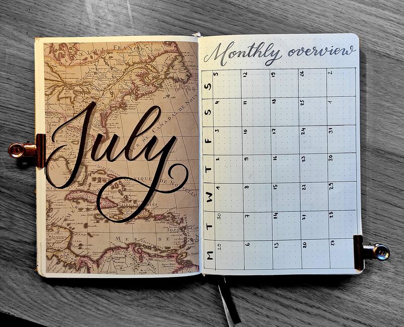 Open bullet journal showing a 'July' vintage map cover page alongside a hand-lettered monthly overview grid