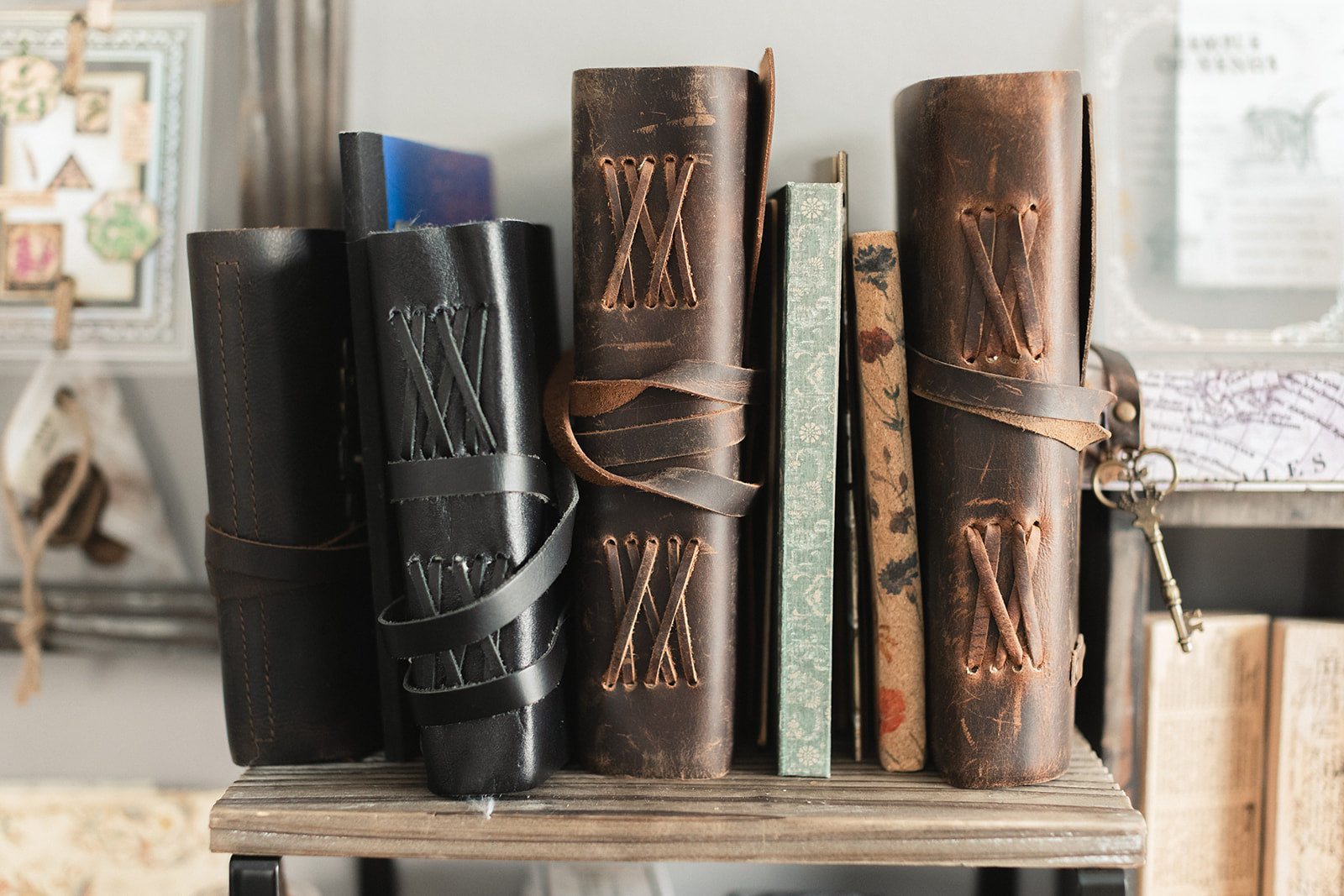 A collection of leather journals standing on a shelf showing different styles — black, dark brown, and medium brown with cross-latch bindings