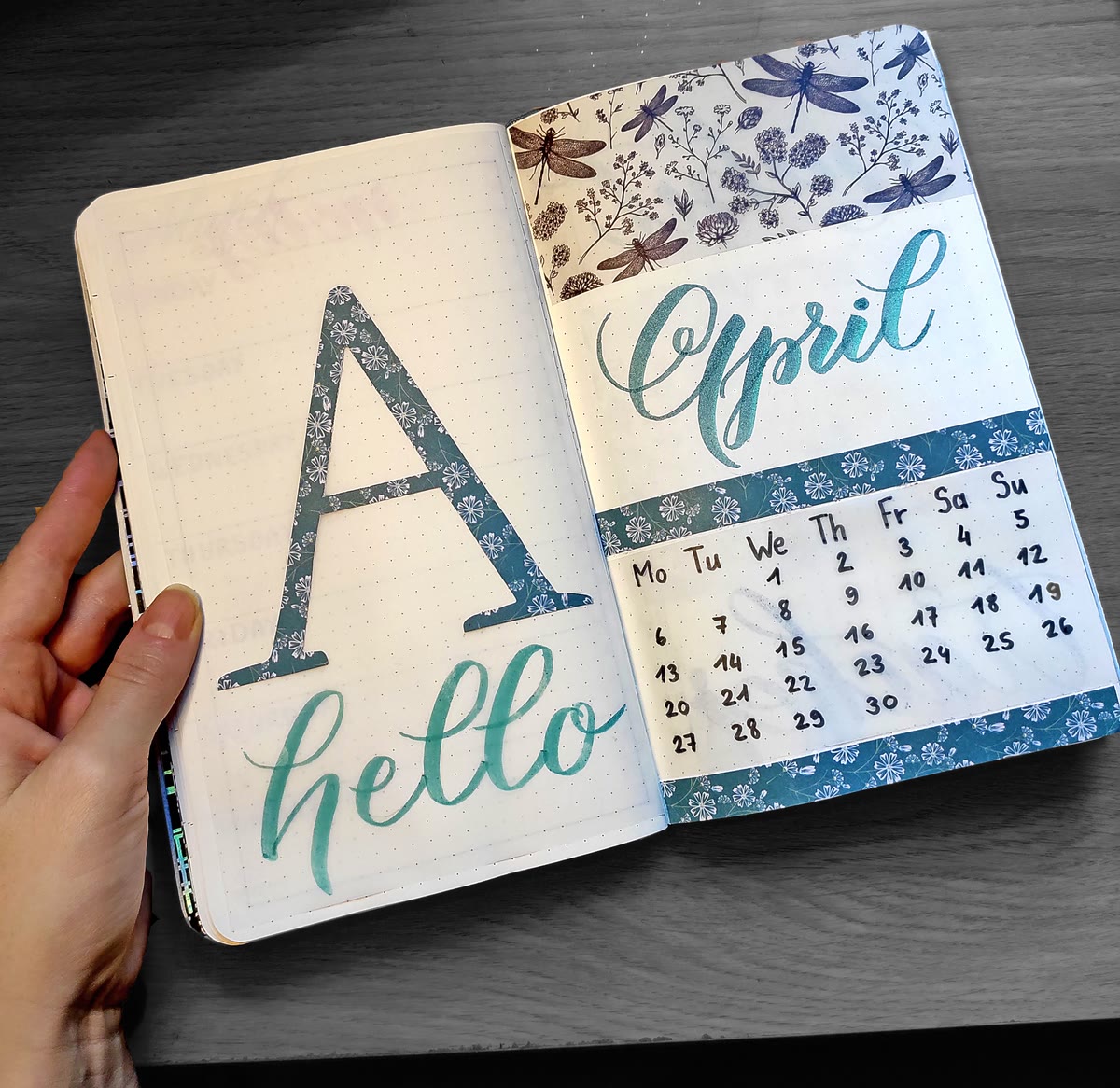 April bullet journal monthly spread — hand-lettered hello April with dragonfly washi tape border and calendar in teal tones